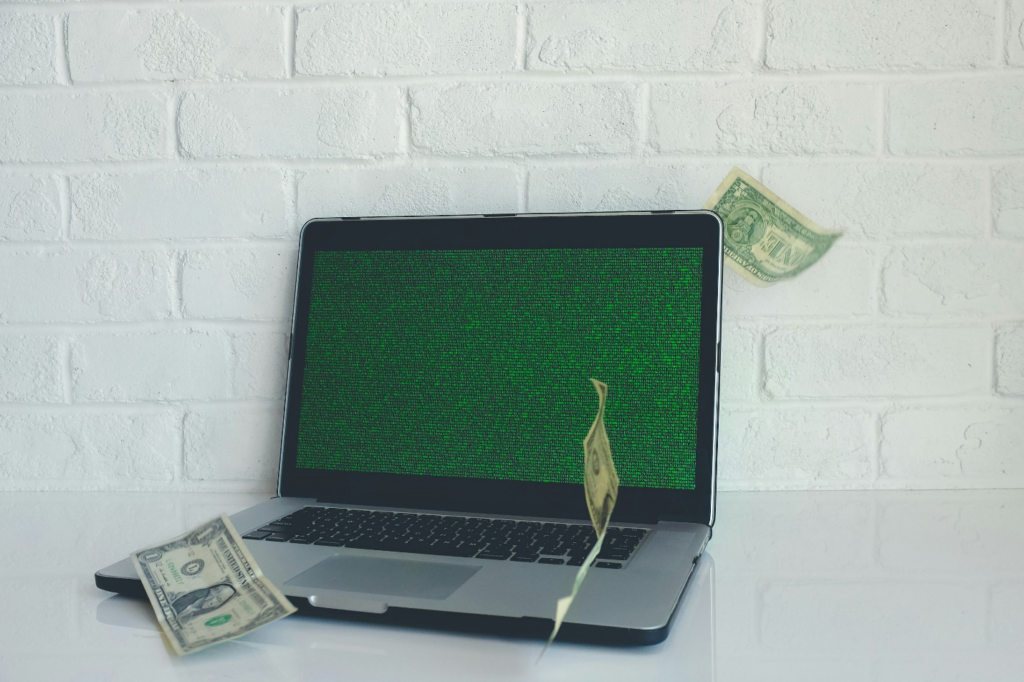 A laptop with a green screen and three-dollar notes falling around it