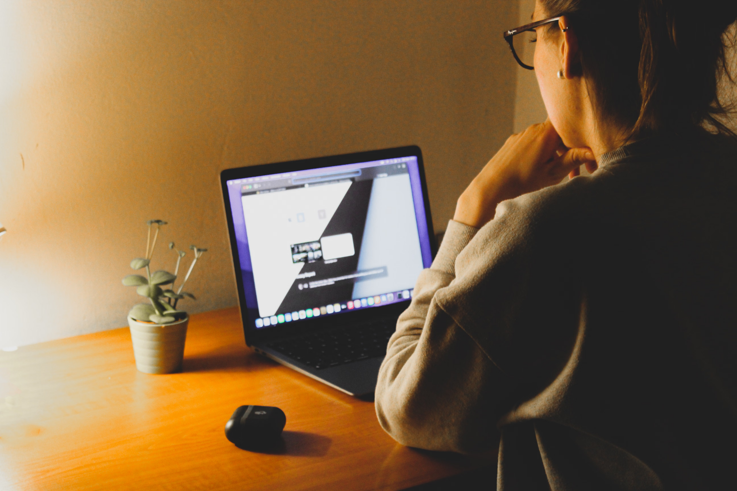 A woman wearing glasses looking at a laptop screen with a thoughtful expression