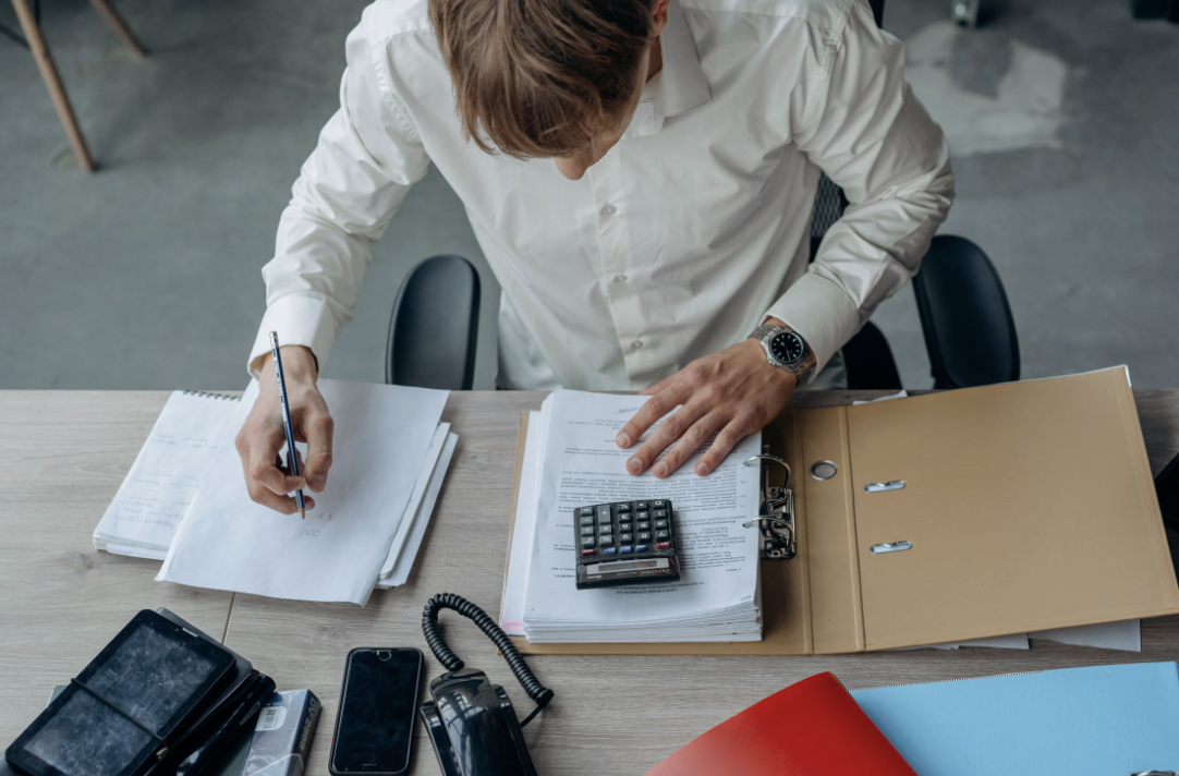 This photo shows a man reviewing printed paperwork at an office desk.