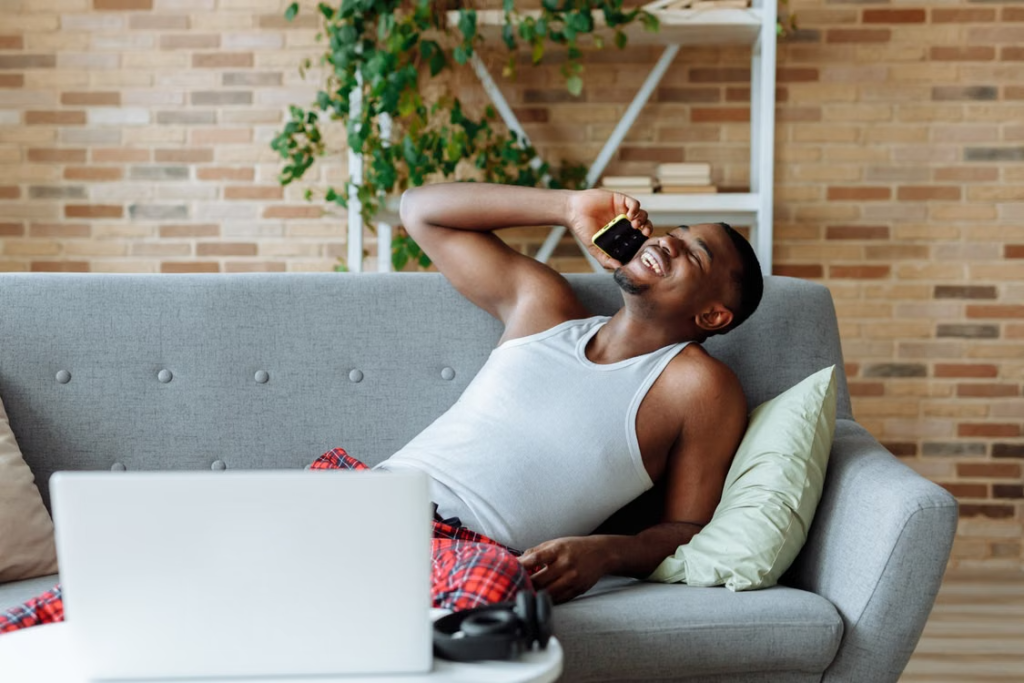 A man relaxed on a couch while using a mobile phone.