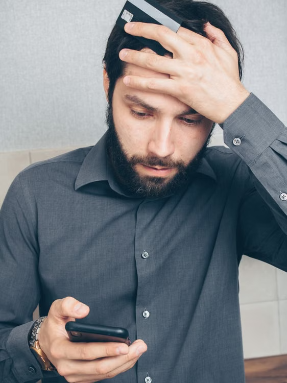 Stressed man checking his smartphone while holding a credit card during a suspected scam call